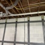 View of a ceiling under construction, featuring insulation, piping, and ductwork, with invisibeam foundation support straps marking grid-like patterns.