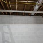 Basement wall with a visible crack, featuring exposed pipes above and a wooden support structure.