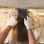 A worker in white gloves adheres Invisibeam to a textured wall during a renovation project.