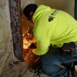A construction worker in a bright yellow jacket cuts through metal, creating sparks, while working on a renovation project.