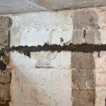 A worker applies cement to a partially finished wall, showcasing uneven surfaces and grey concrete blocks in a dimly lit basement.