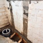 View of a basement corner with exposed concrete blocks, a drainage pipe, and fresh cement along the floor, indicating renovation work.