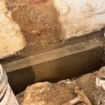 A freshly poured concrete slab in a construction site, surrounded by dirt, debris, and a construction bucket.